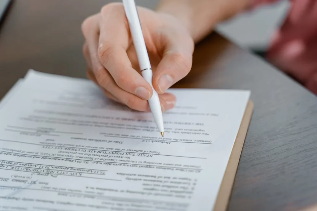 Close-up of a person filling out an official immigration form with a white pen, representing an expat reporting changes to Czech immigration.